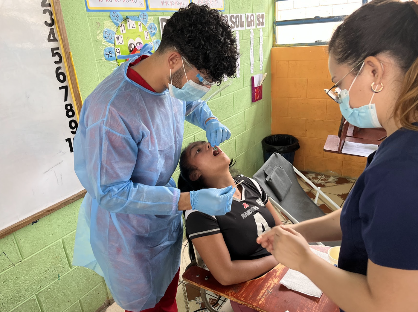 Razi performing oral health care to a young girl with a nurse's help